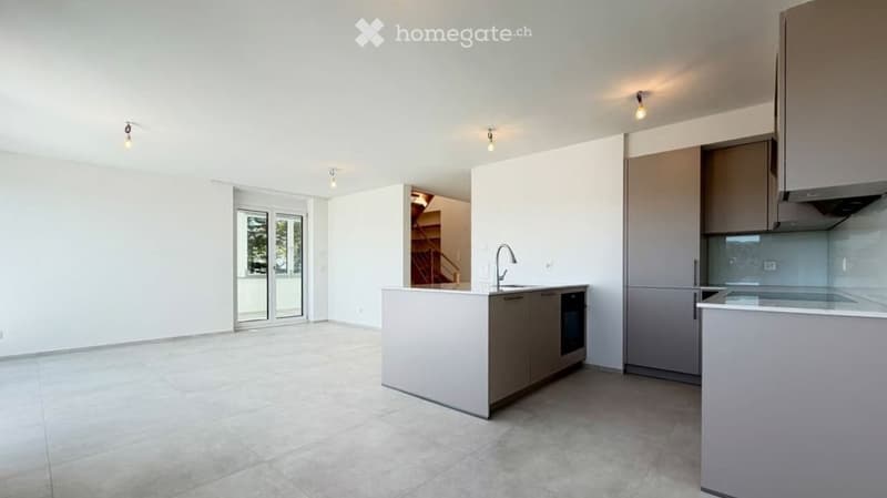Modern, minimalist kitchen with white walls, grey cabinets, and a central island. Features include a refrigerator, oven, sink, and faucet. The space is bright with large windows and recessed lighting.
