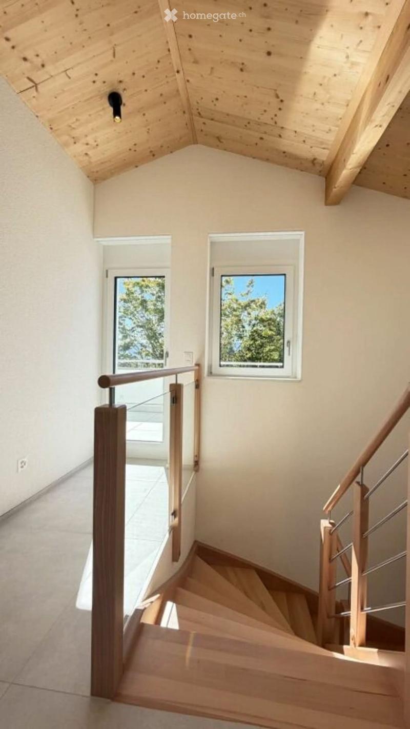 Modern wooden staircase with glass railing, light-colored walls, and skylight windows.