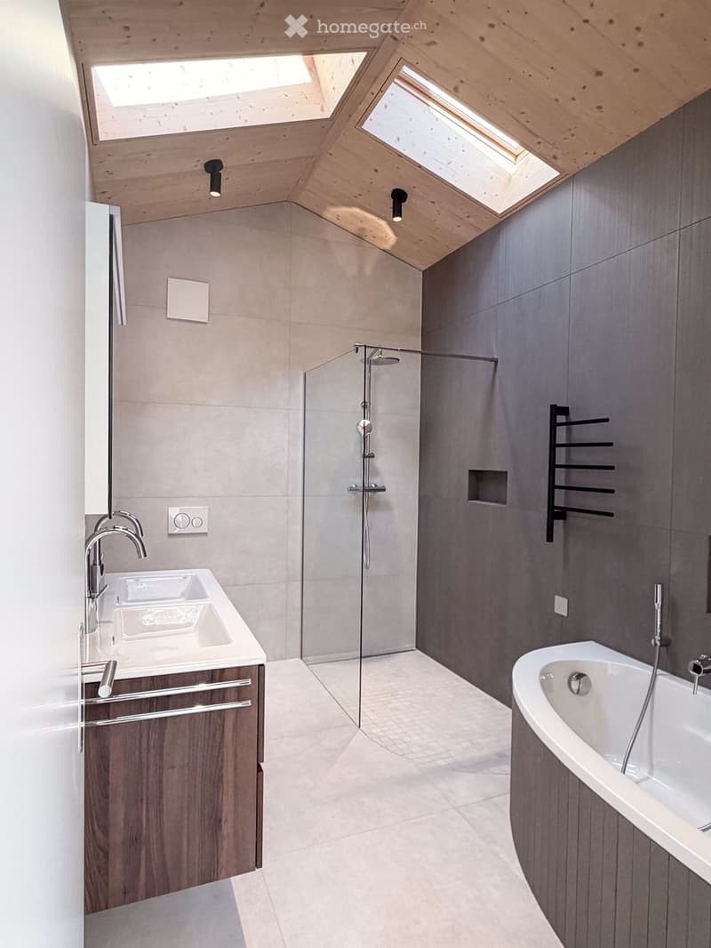 Modern bathroom with a double sink, bathtub, glass-enclosed shower, and sleek wooden cabinetry.