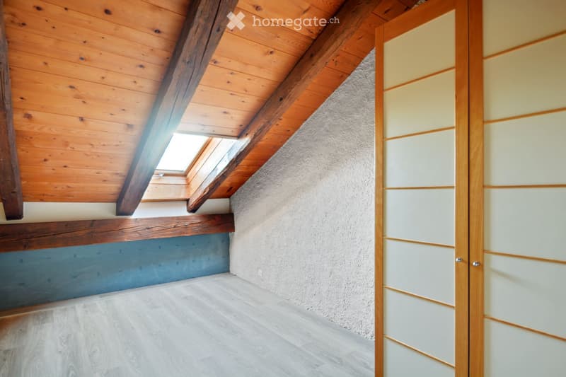 Empty attic space with wooden beams, skylight window, and light-colored wooden flooring.