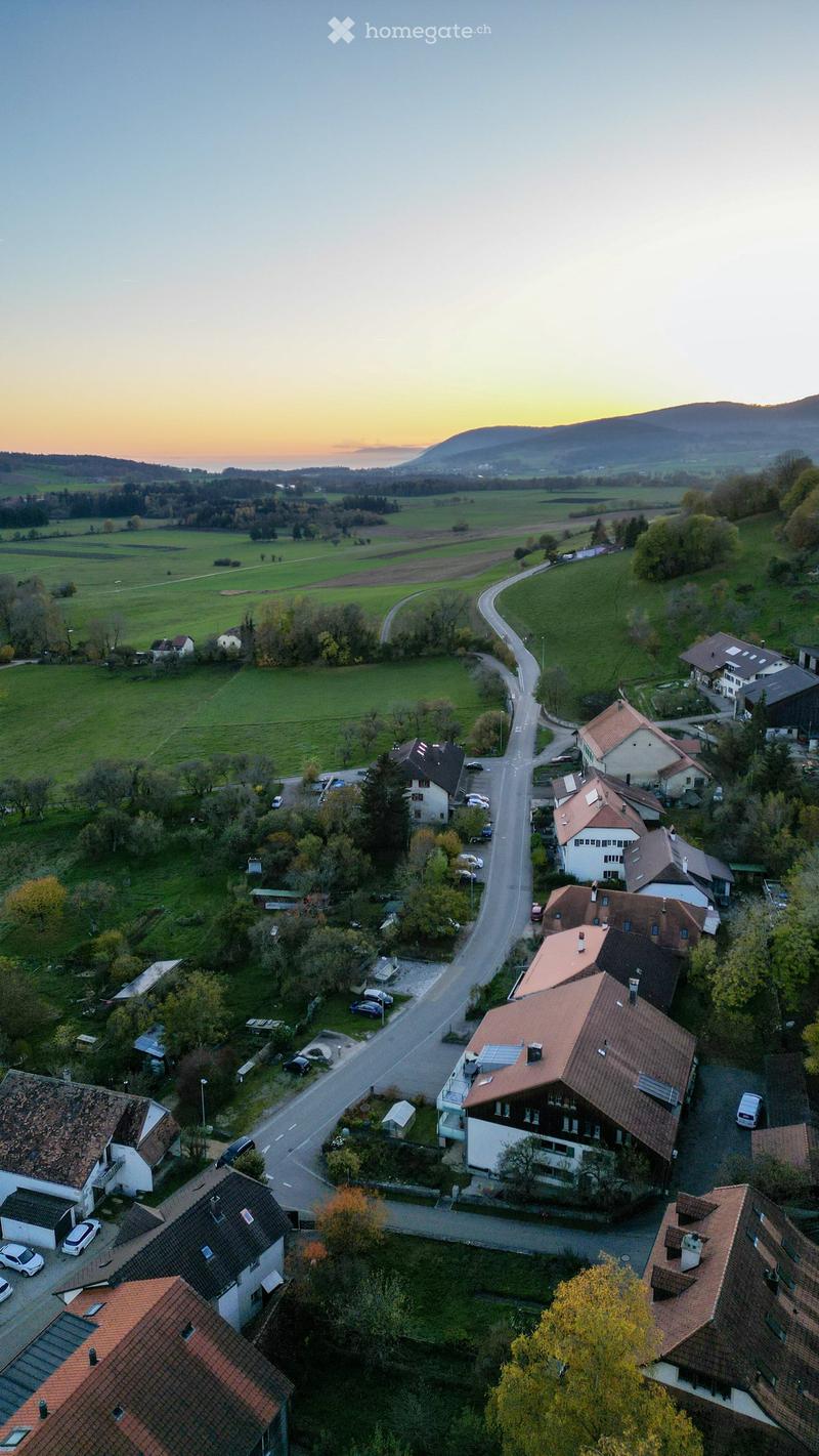 Aerial view of a rural village with houses, roads, and surrounding fields during sunset.