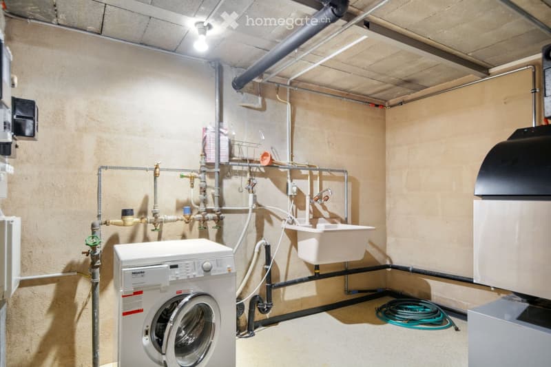 Utility room with a washing machine, sink, and exposed pipes and valves.