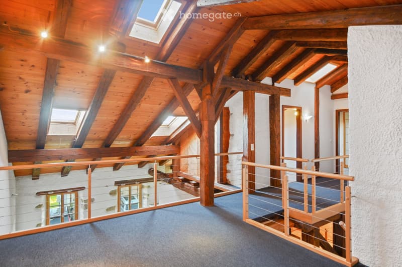 Spacious hallway with exposed wooden beams, skylights, and a wooden railing leading to an upper level.