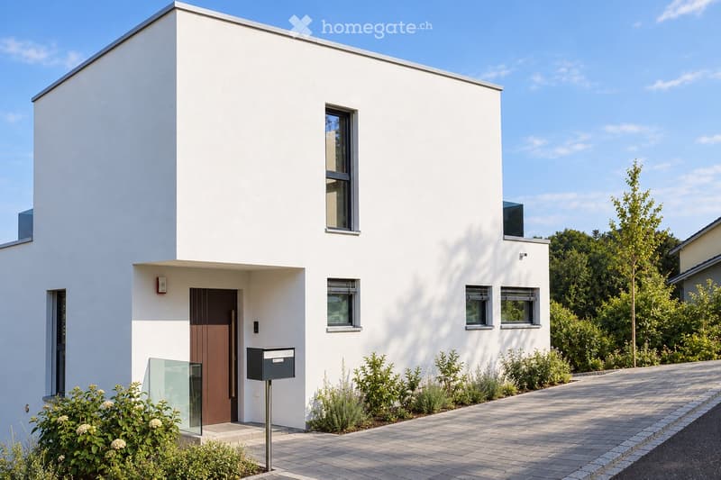 Modern two-story house with white exterior, large windows, and a wooden front door. The house features a clean, minimalist design with a small garden area and a paved pathway leading to the entrance.