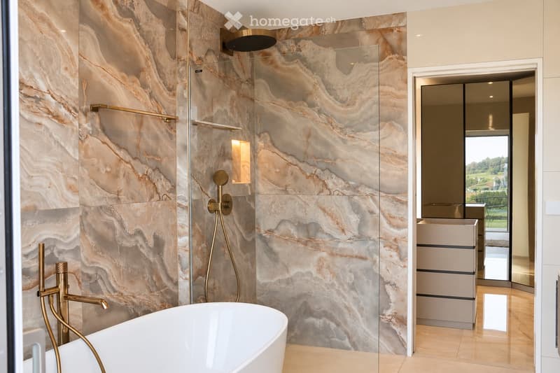 Modern bathroom with marble walls, a freestanding bathtub, gold fixtures, a glass-enclosed shower, and a mirrored vanity with storage.