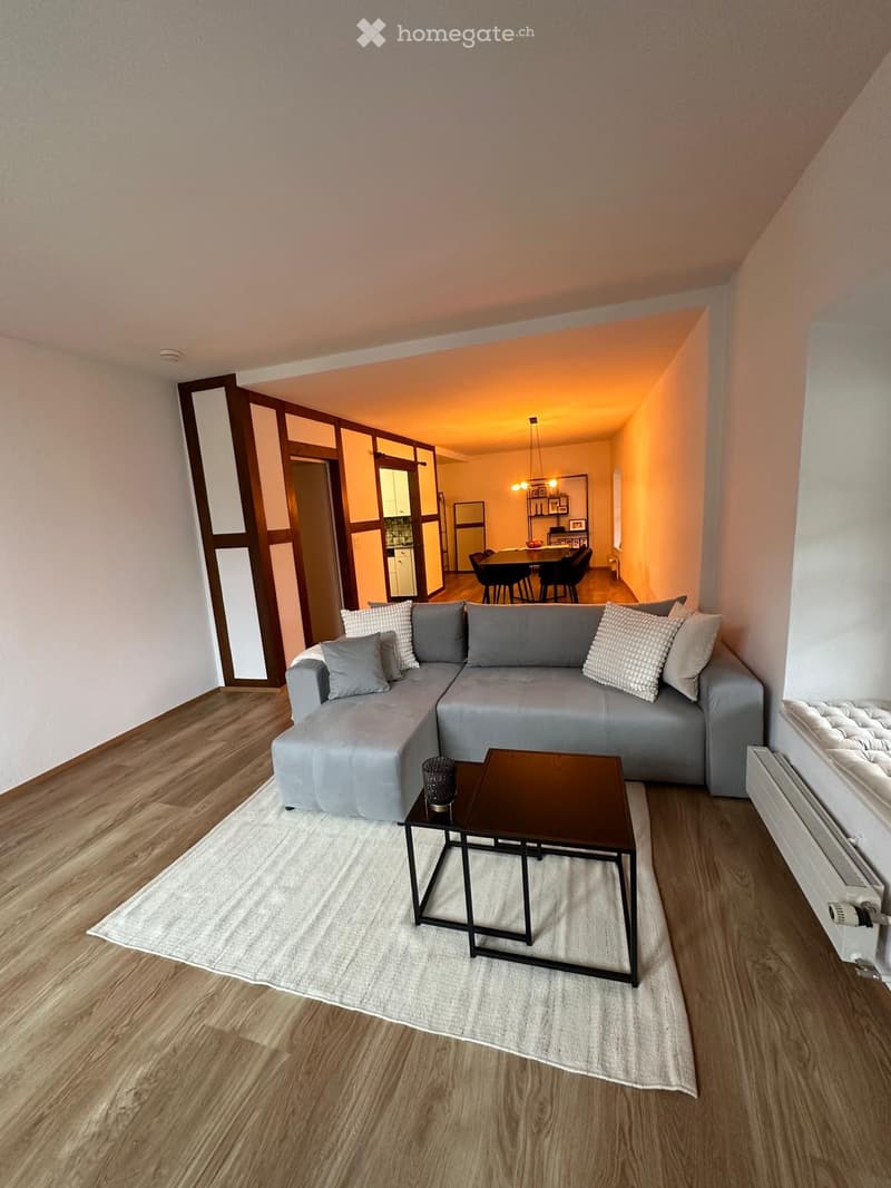 Modern living room with grey sectional sofa, coffee table, dining table, and chairs in the adjacent dining area.