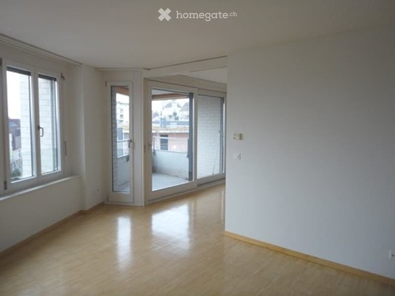 Empty room with wooden flooring, large windows, and sliding glass doors leading to a balcony.