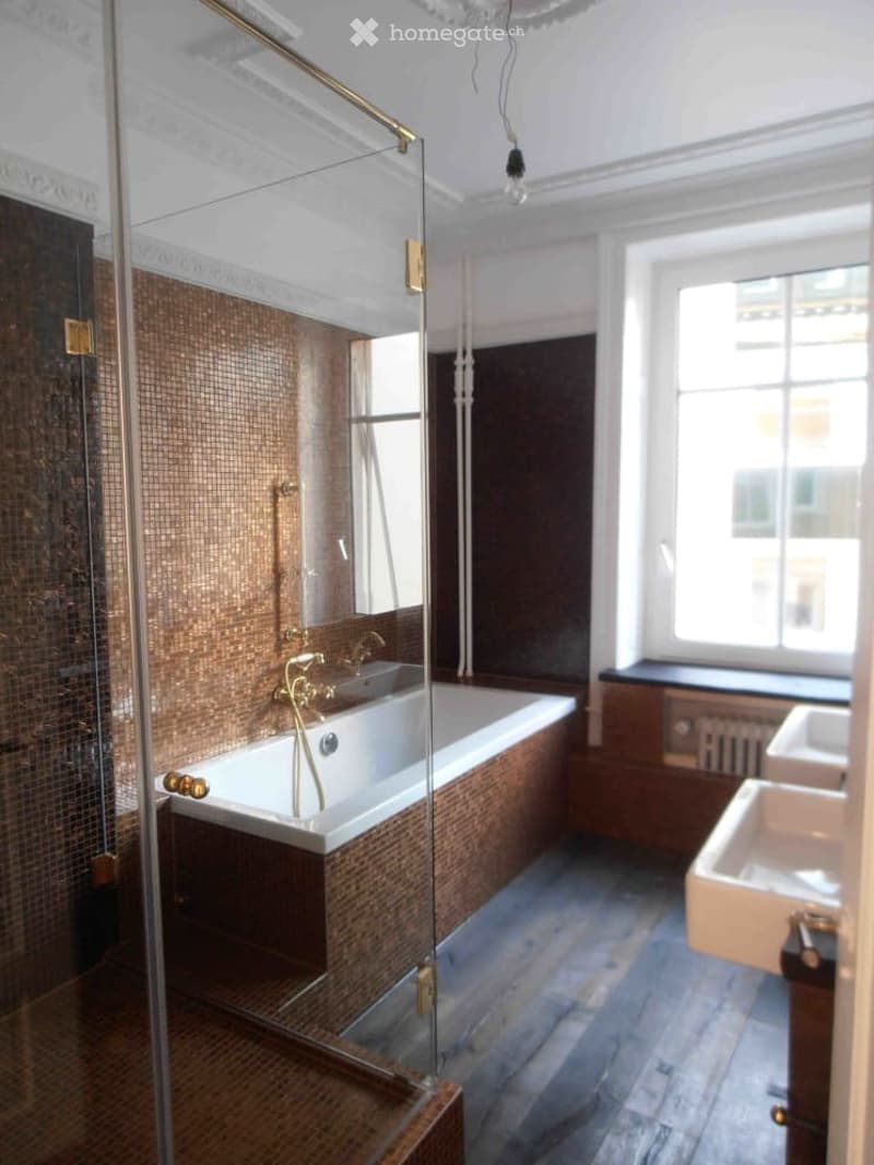 Modern bathroom with a bathtub, sink, and glass shower enclosure. Features dark brown tiles, a wooden floor, and a radiator under the window.