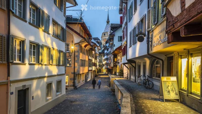 A charming European town street lined with colorful historic buildings, cobblestone pavement, and warm lighting from street lamps.