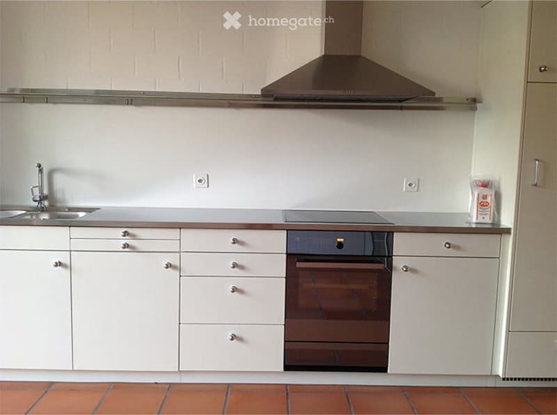 Modern kitchen with white cabinets, stainless steel sink, oven, and range hood. The floor is tiled in orange.