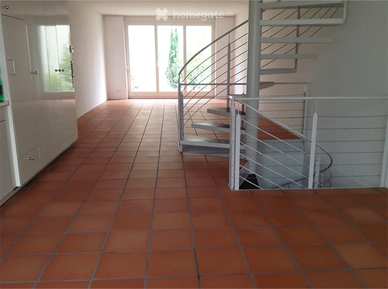 Empty room with terracotta tiled floor, white walls, and a modern spiral staircase leading upwards.