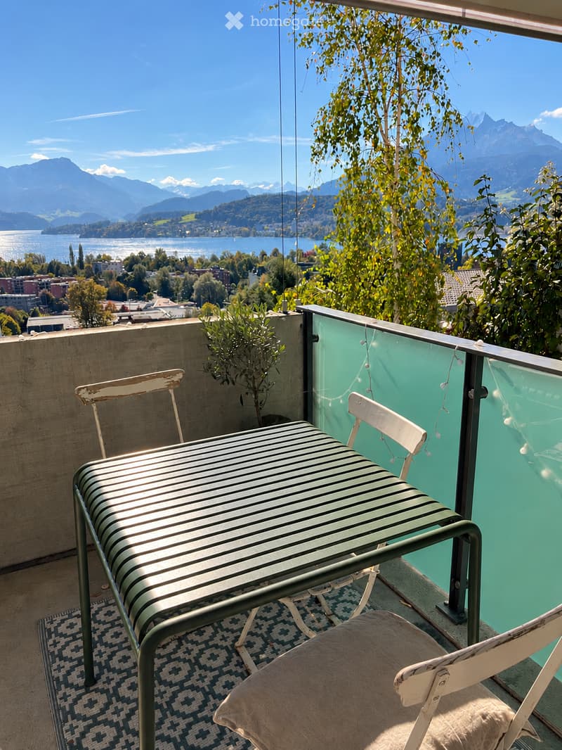 Balcony with a scenic mountain view, featuring a striped table, two chairs, and a patterned rug.