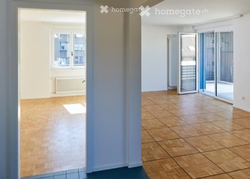 Empty room with wooden flooring, large windows, and sliding glass doors leading to a balcony.