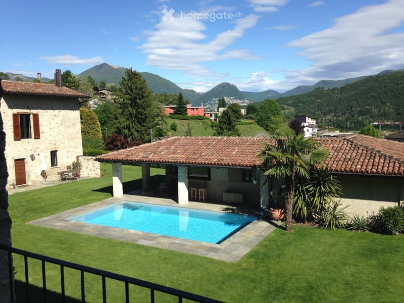 Lush garden with a swimming pool, outdoor seating area, and scenic mountain views.