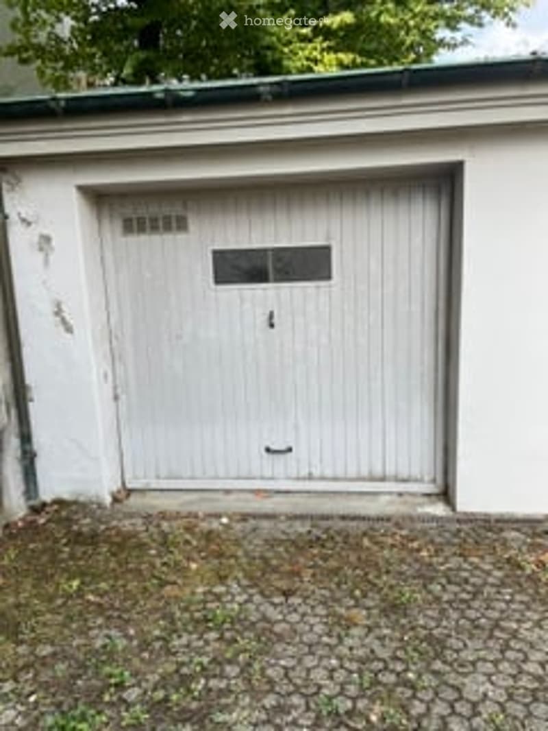 White garage door with a small window and ventilation slots above, situated on a paved area.
