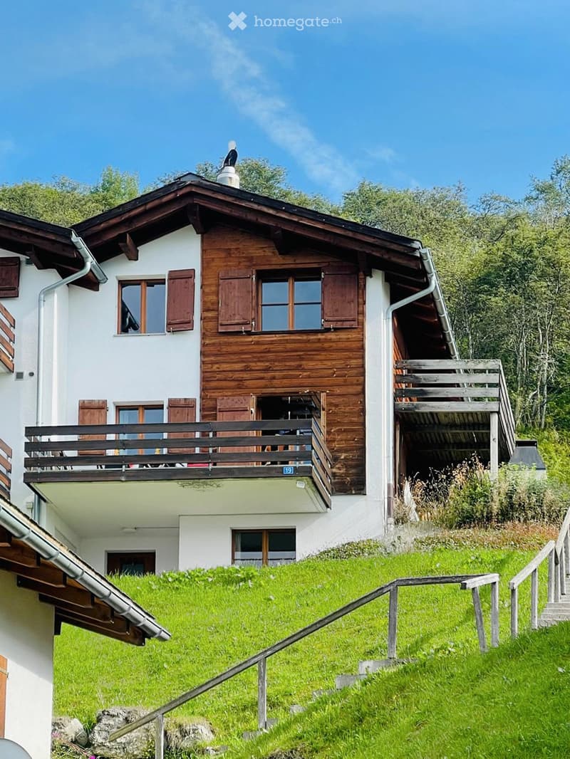 Two-story wooden house with white walls, multiple windows with shutters, a balcony, and a staircase leading up to the house.