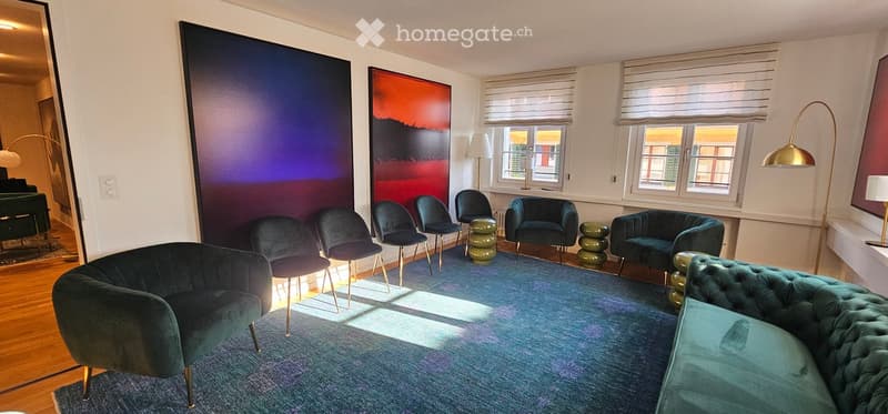 Modern living room with a teal sofa, armchairs, coffee table, floor lamp, and large windows with blinds. Features a blue abstract painting and a large mirror on the wall.