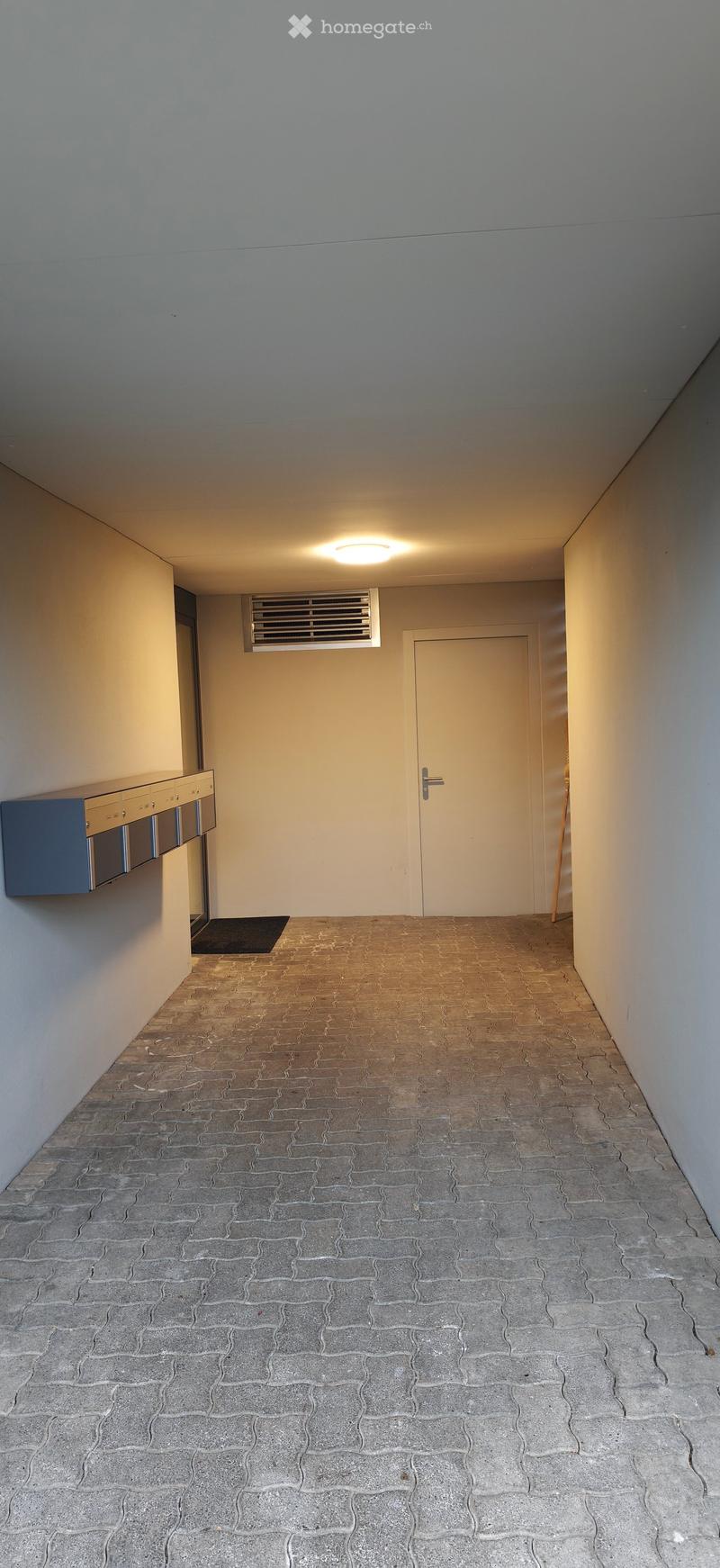Empty hallway with tiled floor, white walls, a closed door, and a small cabinet on the left side.
