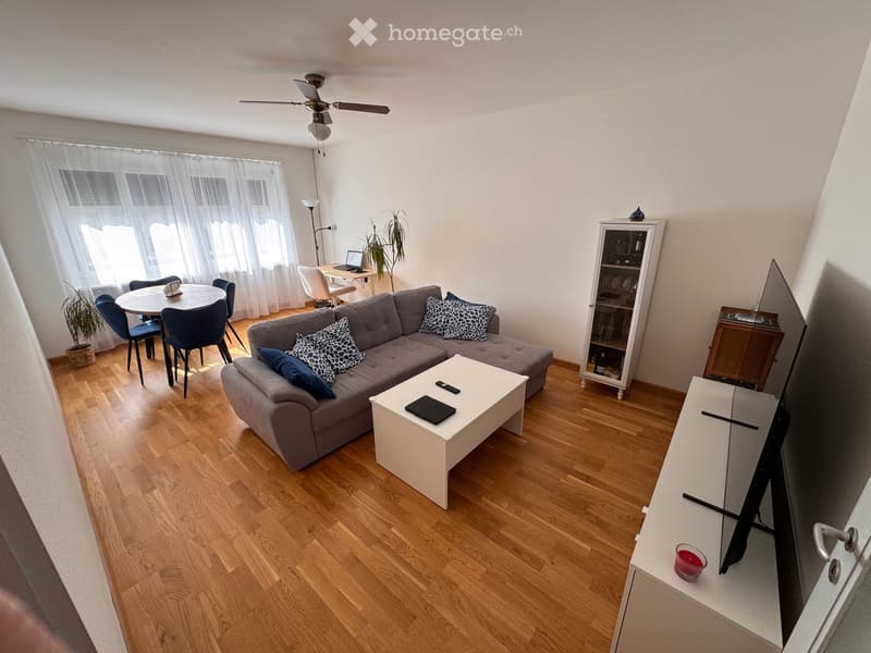A modern living room with a grey sectional sofa, white coffee table, dining area with chairs and table, TV stand, and decorative items.