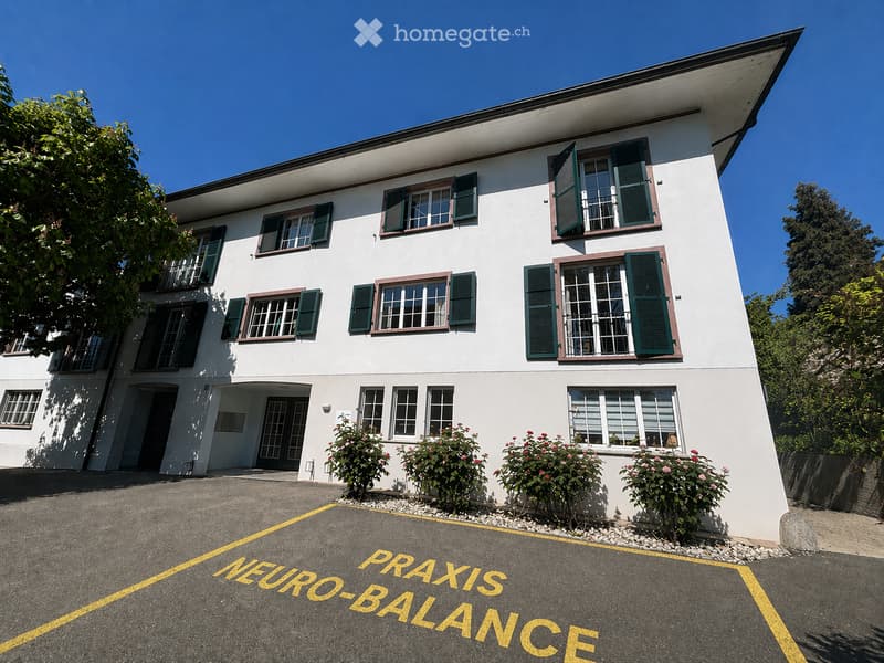 Two-story white building with green shutters and multiple windows, surrounded by greenery and a parking area marked "NEURO-BALANCE".