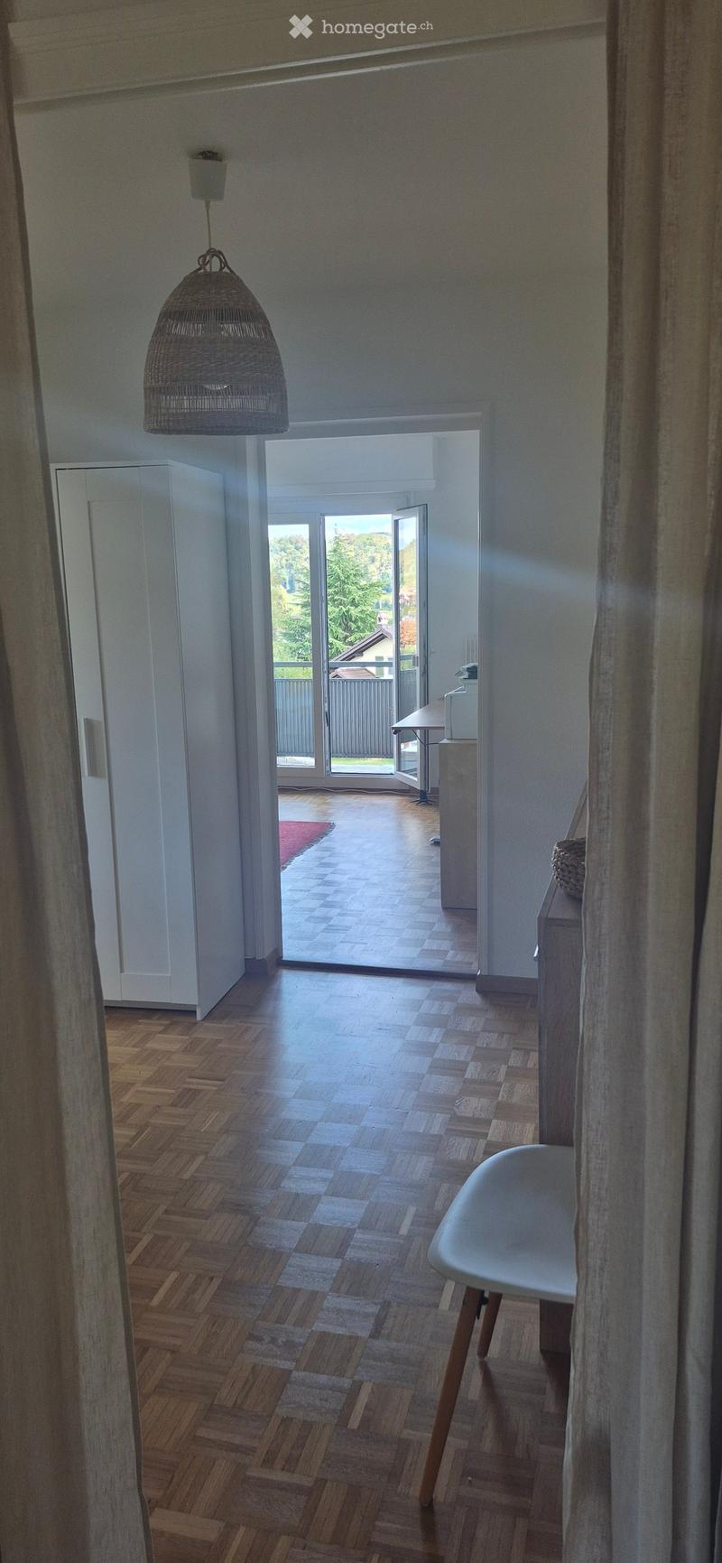 Bright hallway with wooden herringbone flooring, white walls, large sliding glass doors leading to outdoor area, pendant light fixture, and a white chair visible.