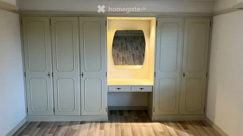 Built-in closet with a small desk and mirror, featuring soft lighting and wooden flooring.