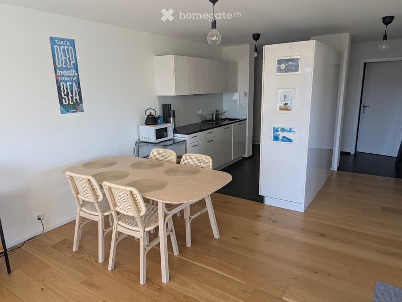 A modern kitchen and dining area with a wooden dining table, four chairs, white cabinets, a microwave, and a sink.
