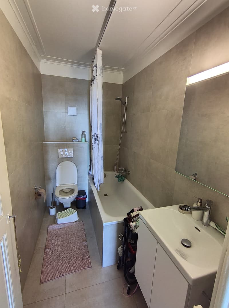 Compact bathroom with a toilet, bathtub, sink, and mirror. Includes a shower curtain, bathroom rug, soap dispenser, and a small stool.