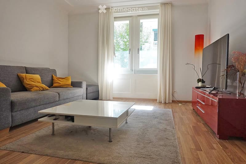 Modern living room with grey sofa, white coffee table, red TV stand, floor lamp, and decorative vase on TV stand.