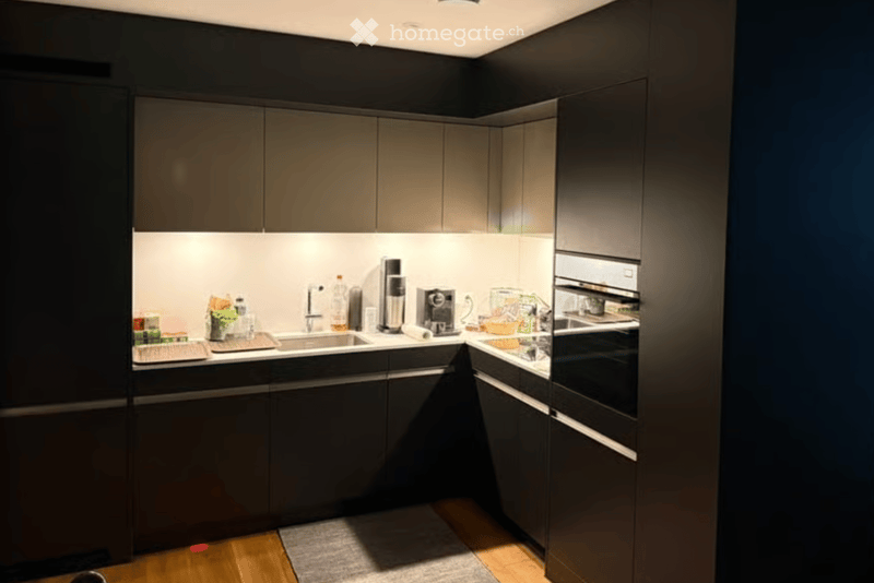 Modern kitchen with dark grey cabinets, stainless steel appliances, and a sleek design. Includes a sink, coffee maker, and oven.