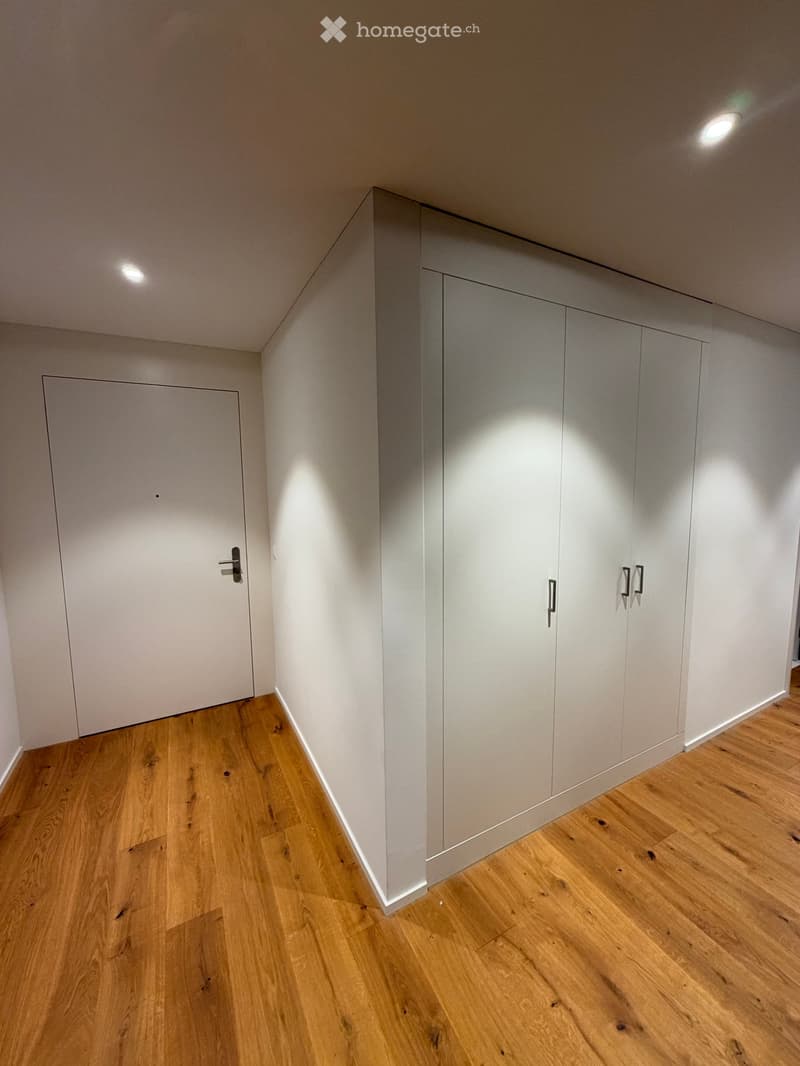Empty room with light wooden flooring, white walls, built-in wardrobes, and a closed door.