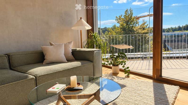 Modern living room with a grey sofa, glass coffee table, table lamp, potted plant, and a view of the city from a large balcony.
