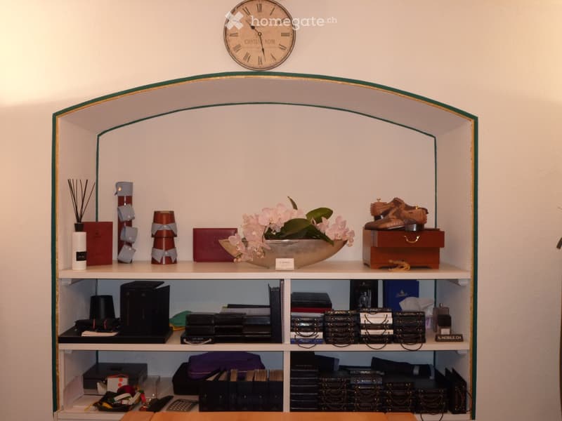 A well-organized shelf unit with a variety of decorative items, including a clock, a vase with flowers, a wooden box, books, candles, and other decorative pieces.