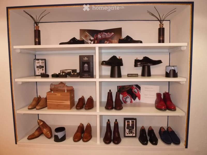 A display shelf unit with multiple pairs of shoes, decorative items, and framed pictures arranged neatly on white shelves.