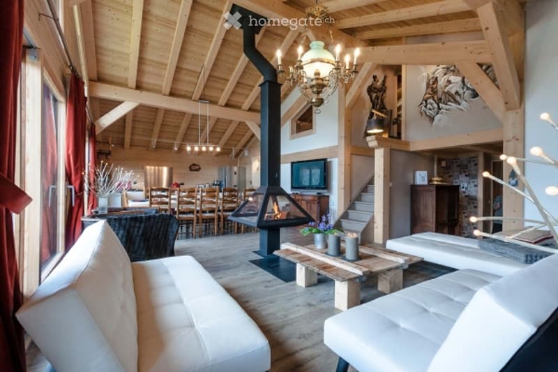Spacious living room with exposed wooden beams, a large fireplace, a white leather sofa, a coffee table, a television, and a dining area with a table and chairs.