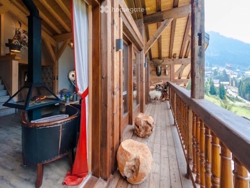 Wooden balcony with a scenic mountain view, featuring wooden railings, stone stools, and a fireplace in the adjacent room.