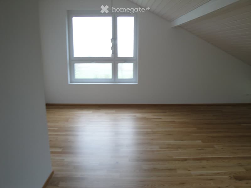 Empty room with wooden flooring and large windows allowing natural light to enter.