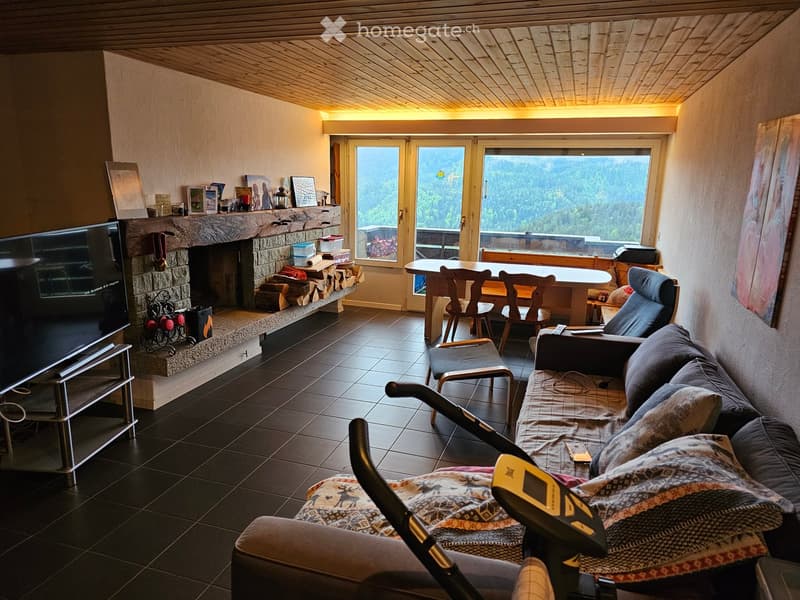 Cozy living room with a stone fireplace, large windows offering a scenic mountain view, a sofa, coffee table, chairs, and a dining table with chairs.