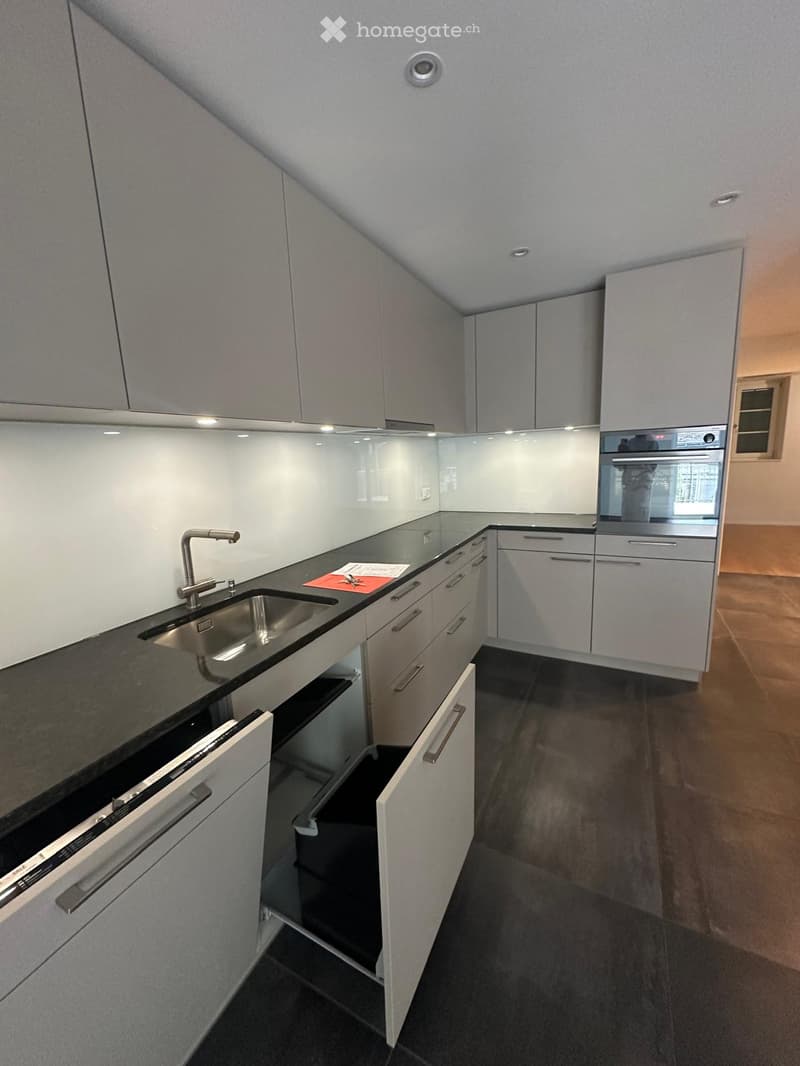 Modern kitchen with white cabinets, black countertops, stainless steel sink, and built-in oven. Features include a sleek design with ample storage space and a contemporary aesthetic.