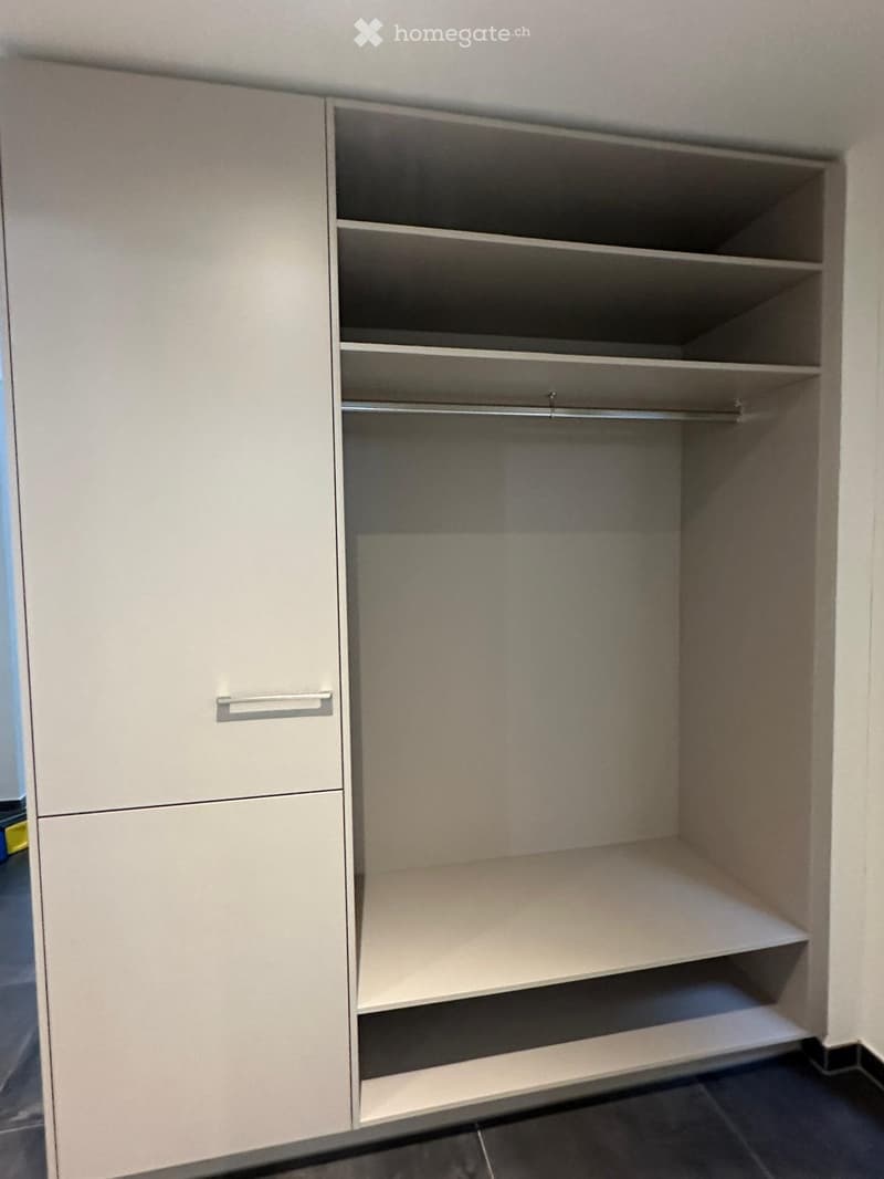 Empty closet with beige walls, shelves, and a hanging rod, no items inside.