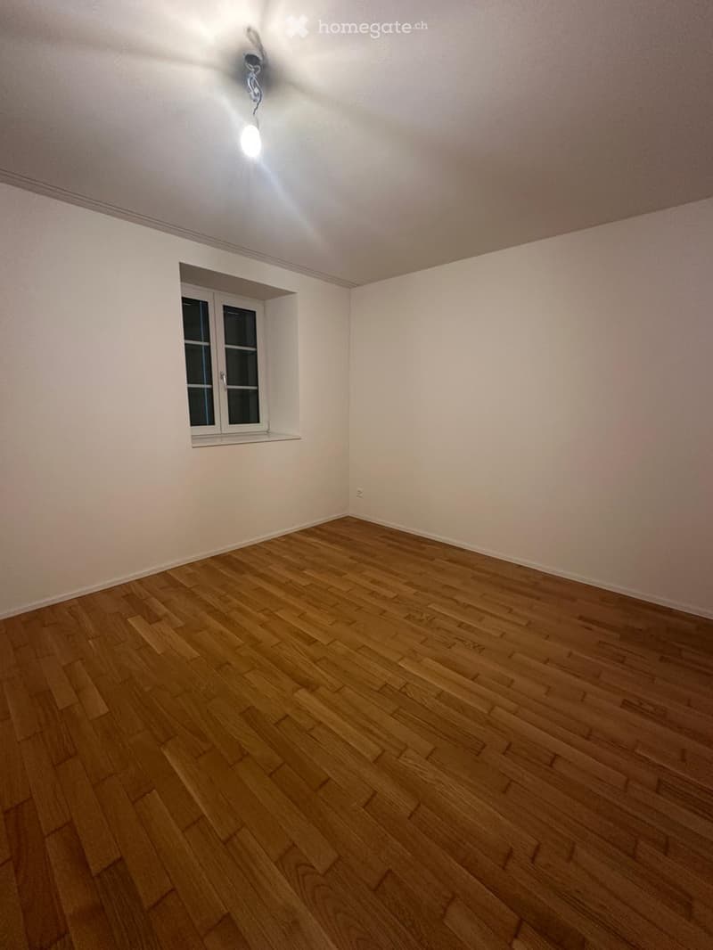 Empty room with wooden flooring, white walls, and a single window with double glass panes.