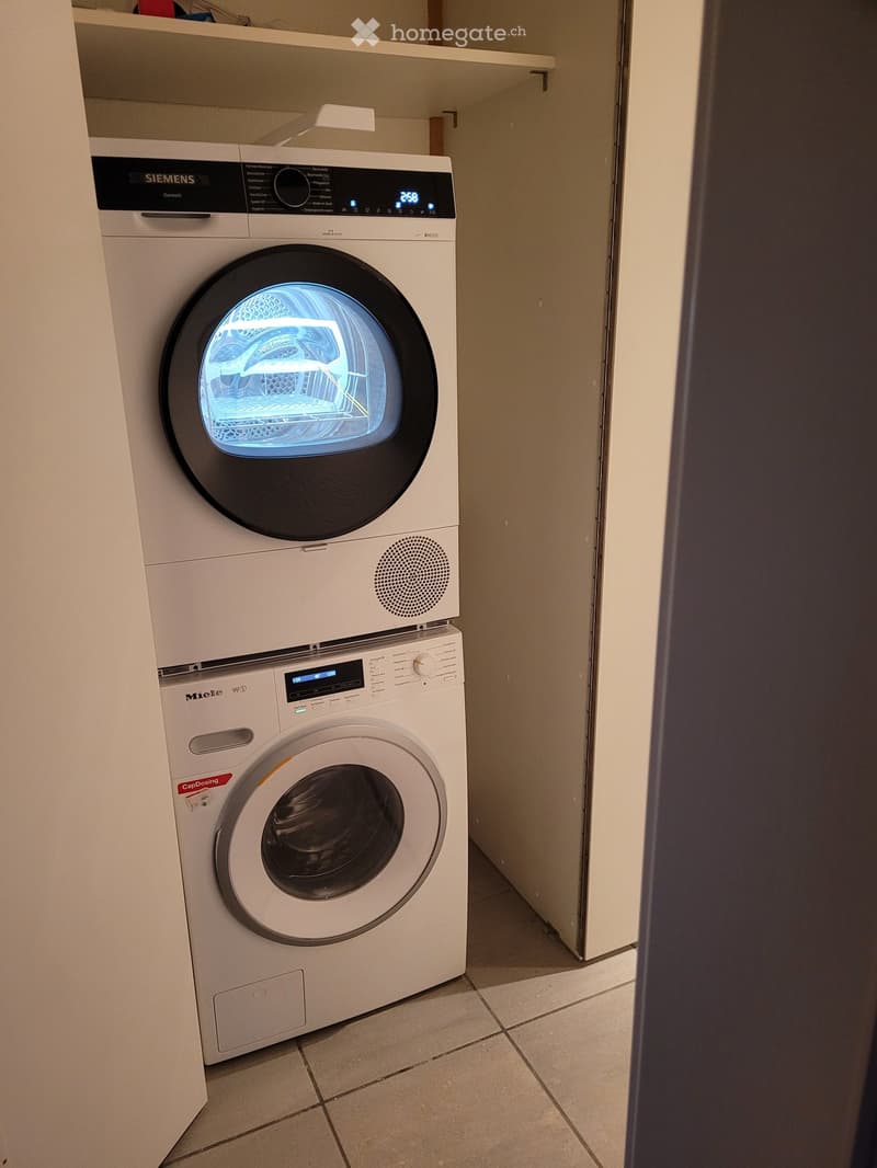 A compact bathroom with a stacked washing machine and dryer unit, featuring modern digital displays and sleek design.
