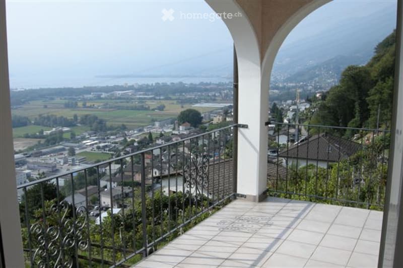 Outdoor balcony with tiled floor, black railings, panoramic view of the town and mountains.