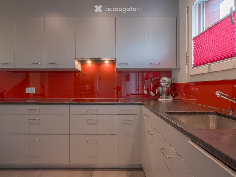 Modern kitchen with grey cabinets, stainless steel sink, stand mixer, and a red backsplash.