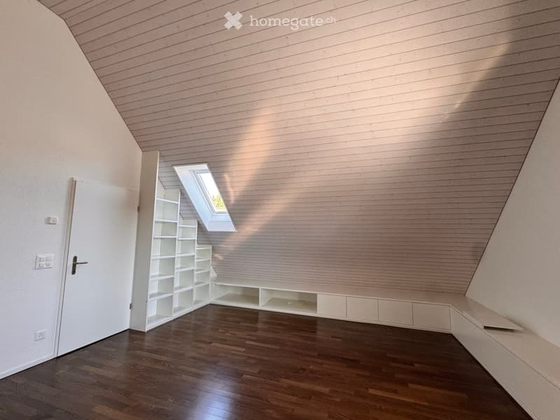 Empty room with wooden flooring, white walls, built-in shelving, and a skylight window.