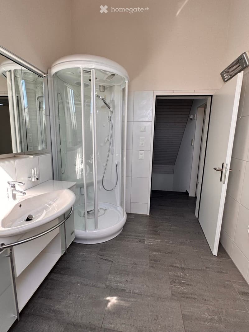 Modern bathroom with a white shower stall, a sink with a mirror, and a tiled floor.
