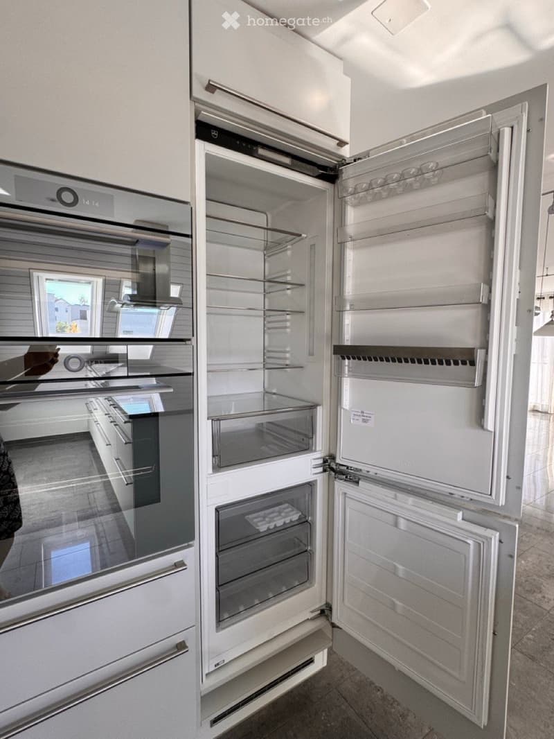 Modern kitchen with stainless steel appliances, including an open refrigerator and oven, sleek cabinetry, and a window view of the exterior.