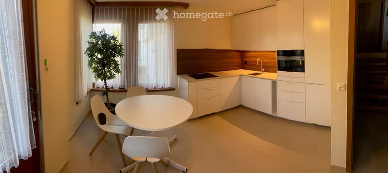 Modern kitchen with white cabinets, a round dining table with chairs, a sink with a faucet, and an oven. A potted plant is placed near the window.