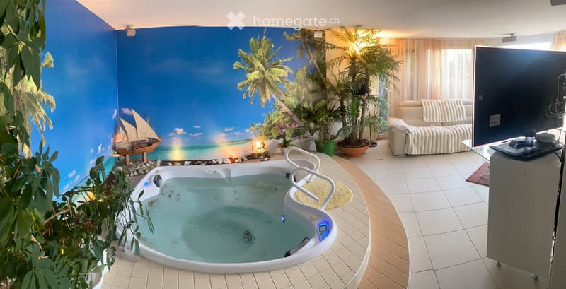A modern living room with a large hot tub, a sofa, a television, and several potted plants, featuring a beach-themed mural on the wall.