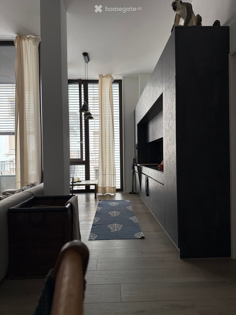 Open-plan living and kitchen area with modern dark wood cabinets, a sofa, a small table with chairs, and a blue patterned rug.